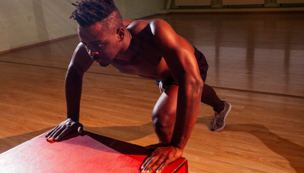 afro man pushing up on the floor in dark light gym in evening.